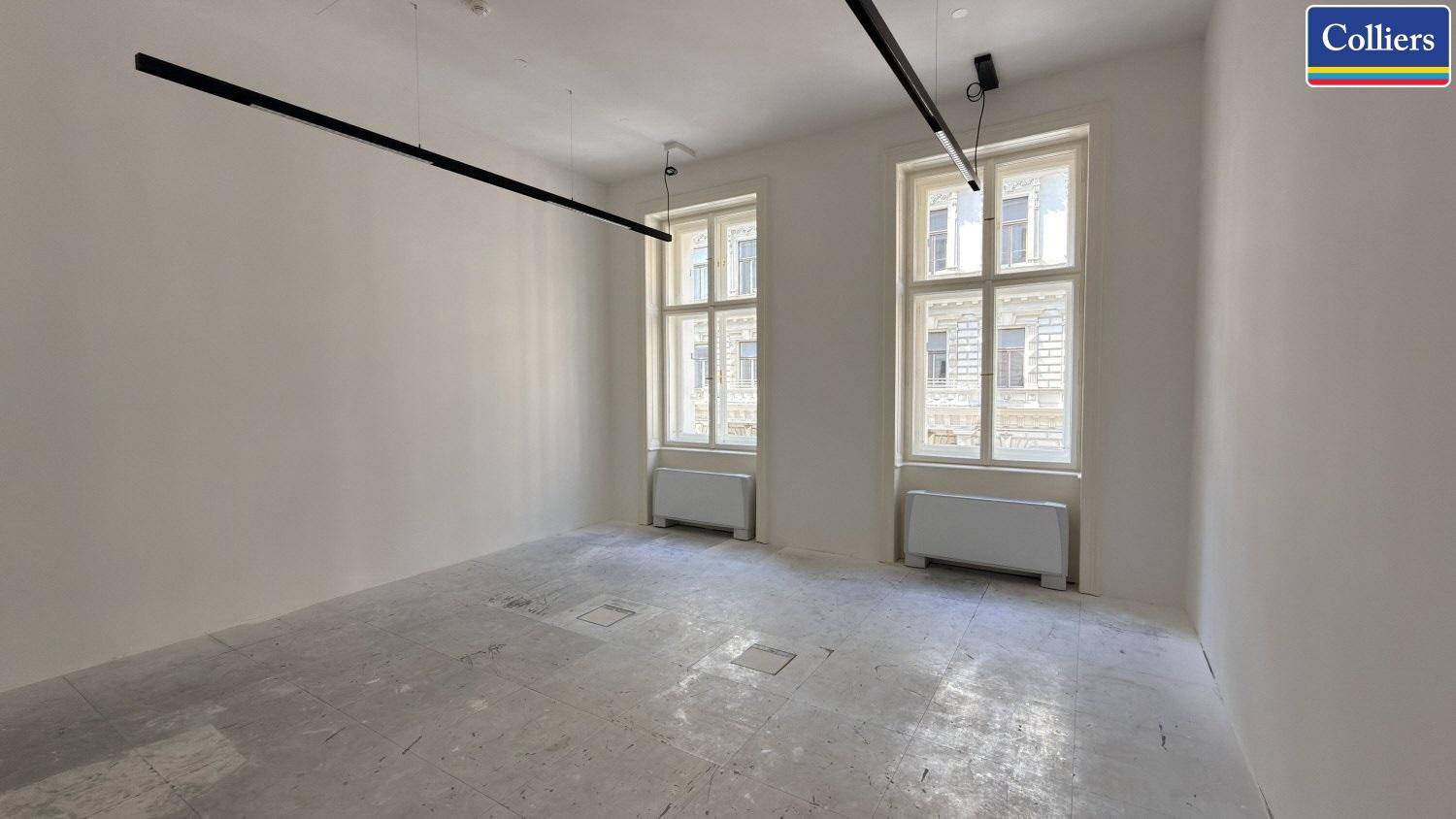 Geräumiger Büroraum mit zwei großen Fenstern und moderner Deckenbeleuchtung.