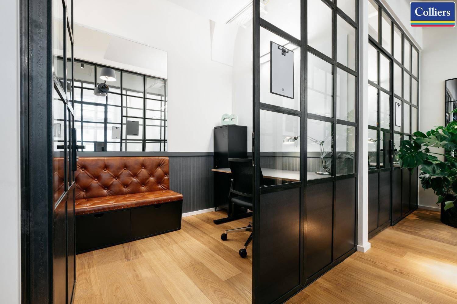 Moderner Bürobereich mit Glasabtrennungen, Holzboden und einer bequemen Lederbank.