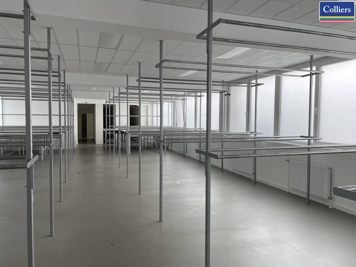 Großer, heller Innenraum mit funktionalen Metallregalen und großen Fenstern, ideal für Bürozwecke.