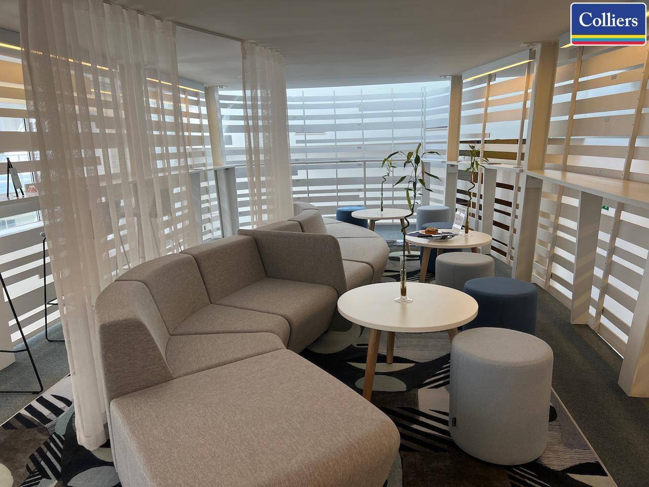 Gemütlicher Loungebereich mit geschwungenem Sofa, kleinen Tischen und großen Fenstern für viel Tageslicht.