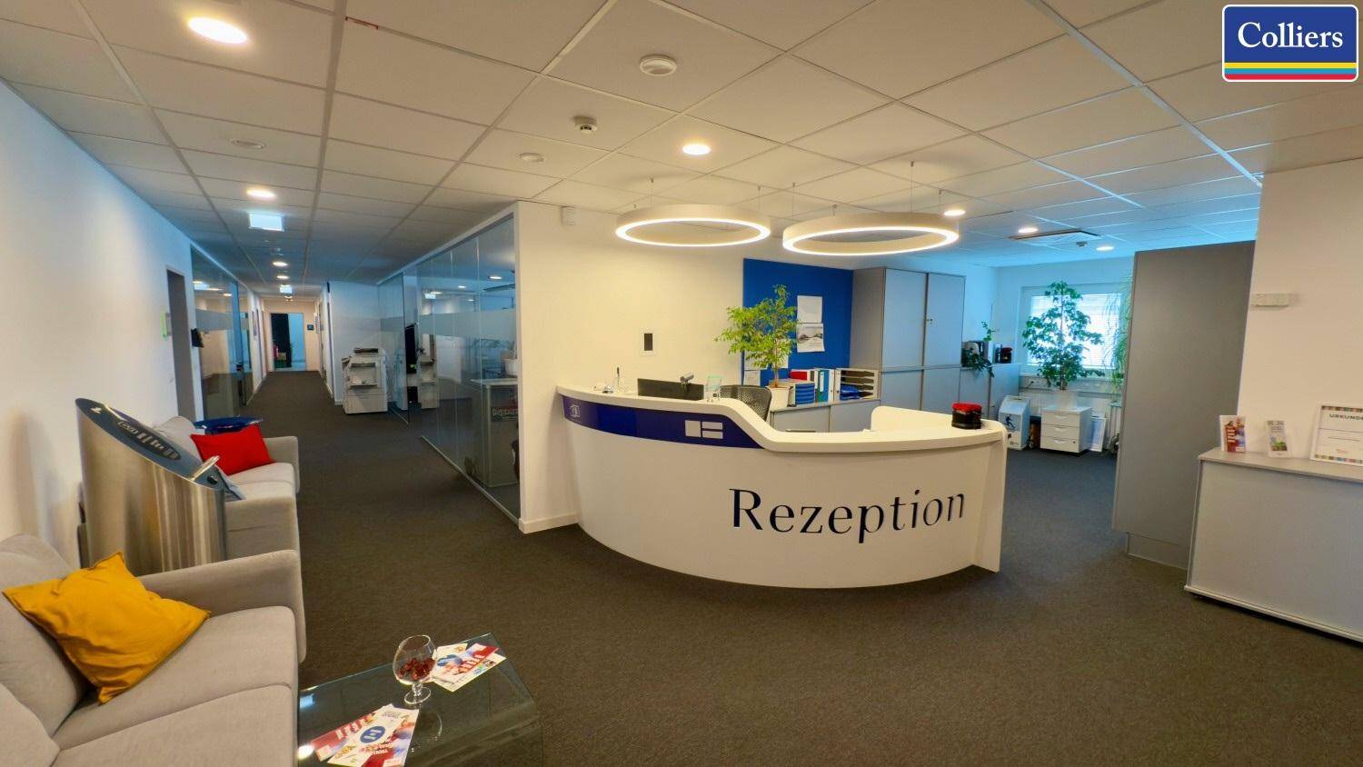 Geräumiger Empfangsbereich mit moderner Rezeptionstheke, Sitzgelegenheiten und Teppichboden.