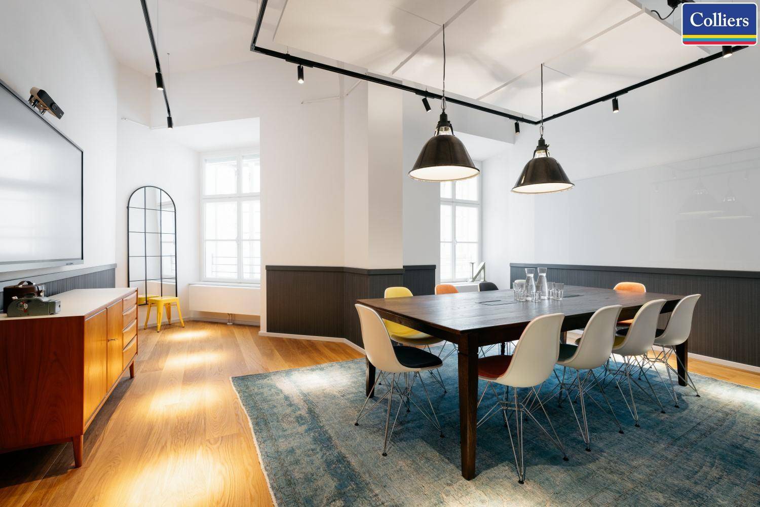 Moderner Besprechungsraum mit großem Holztisch, Designstühlen und einem großen Bildschirm.