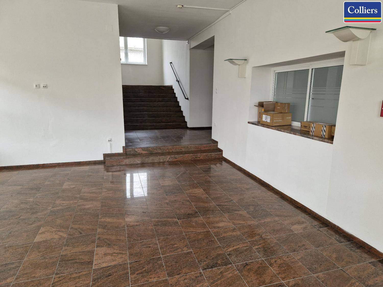 Eingangsbereich mit braunen Fliesen, einer Rezeption und einer Treppe zum Obergeschoss.