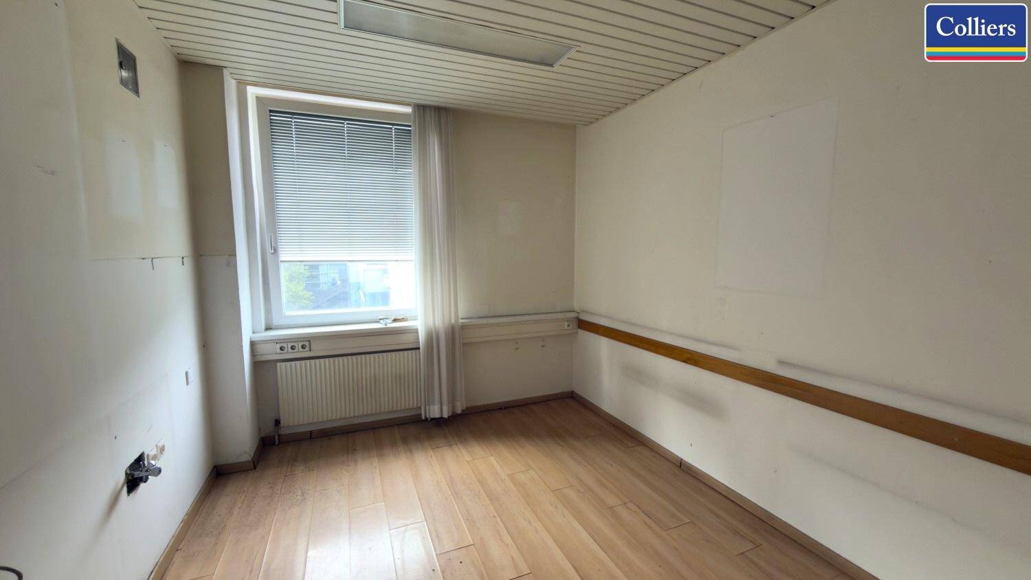 Kleiner Büroraum mit Holzparkettboden, einem Fenster und einfacher Ausstattung, der eine Renovierung benötigt.