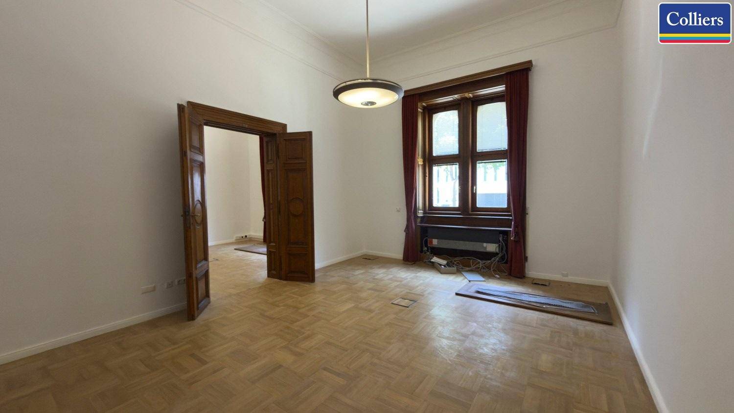 Leerer Raum mit traditionellem Parkett und großen Fenstern, die viel Tageslicht hereinlassen.