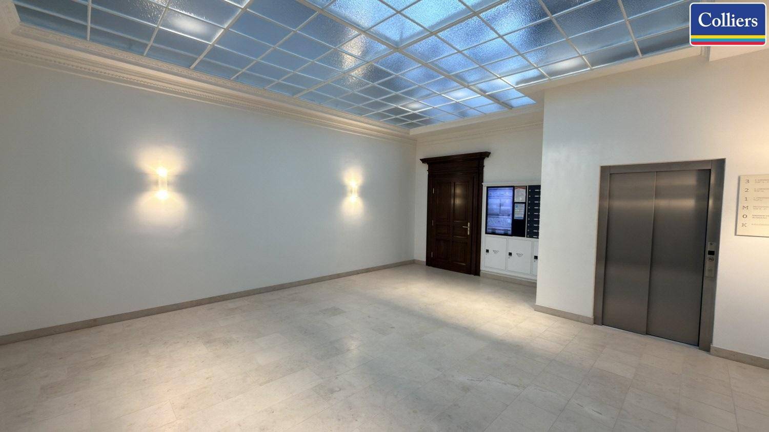 Geräumiger Empfangsbereich mit hellem Fliesenboden, dekorativer Glasdecke und Zugang zum Aufzug.