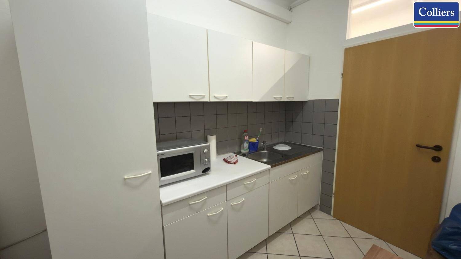 Kleine, funktionale Küchenzeile mit weißen Schränken, Spüle und Mikrowelle, ideal für Pausen.