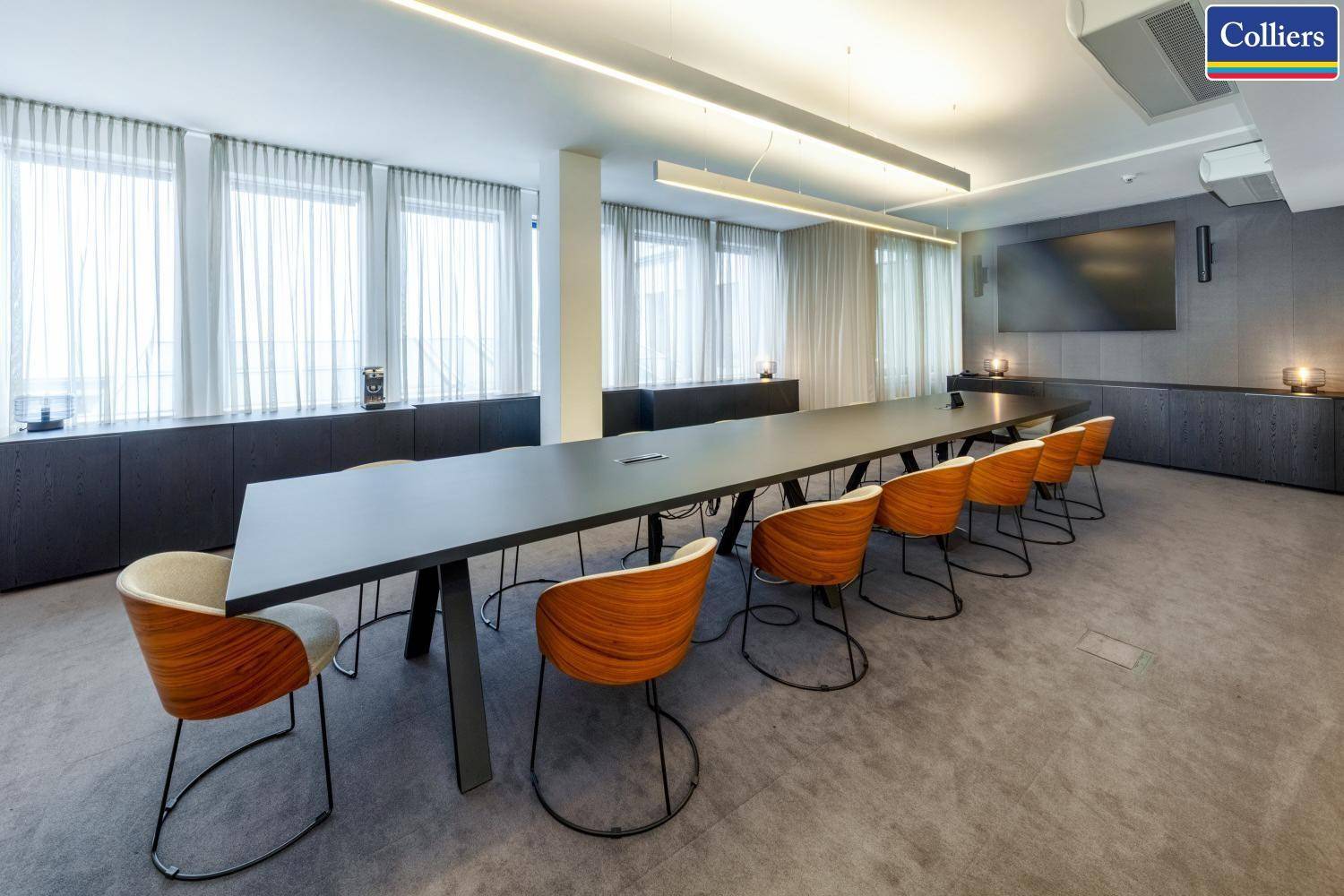 Großer, moderner Konferenzraum mit langem Tisch, bequemen Stühlen und großem Bildschirm.