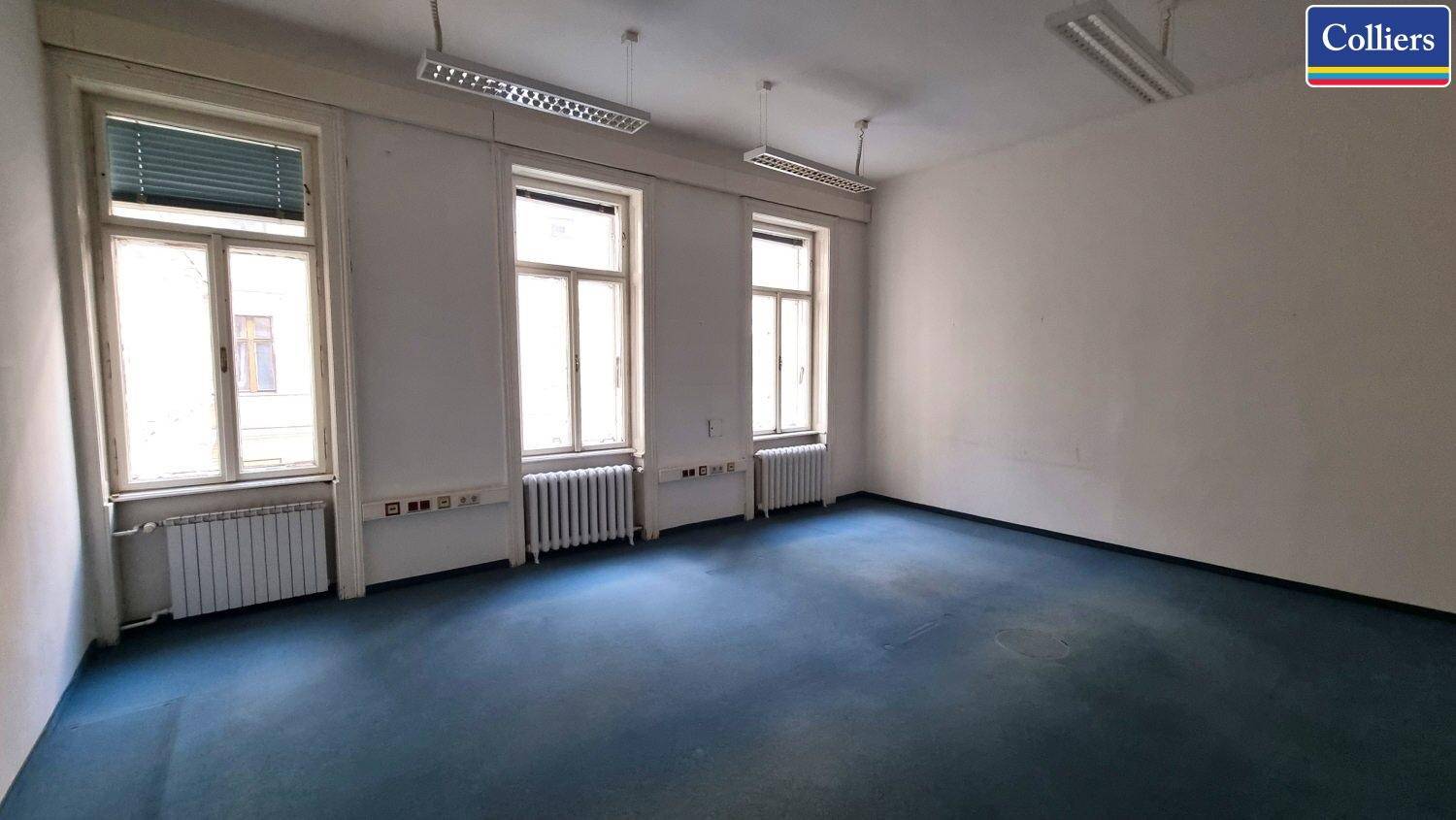 Geräumiges Büro mit blauem Teppichboden, drei Fenstern und Jalousien.