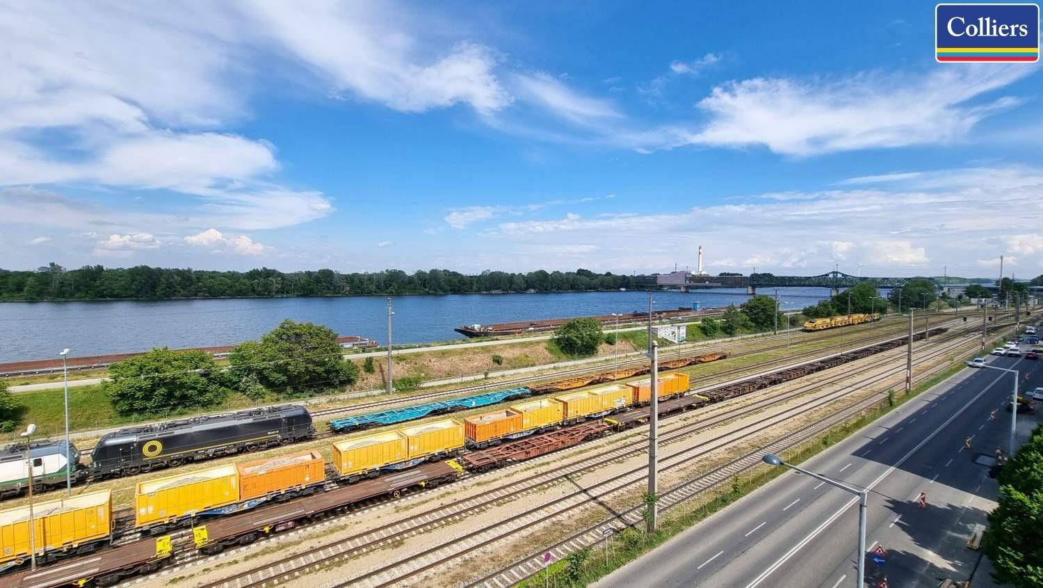 Weitläufige Ansicht des Flusses, Bahngleise und einer Straße unter blauem Himmel mit Wolken.