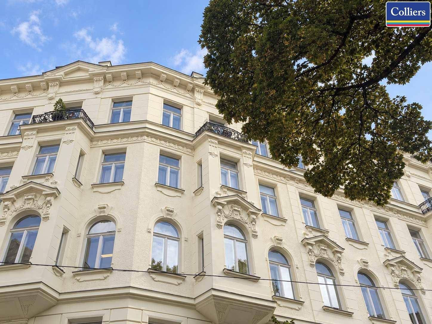 Elegante Fassade eines Altbaus mit verzierten Fenstern und kleinen Balkonen unter blauem Himmel.