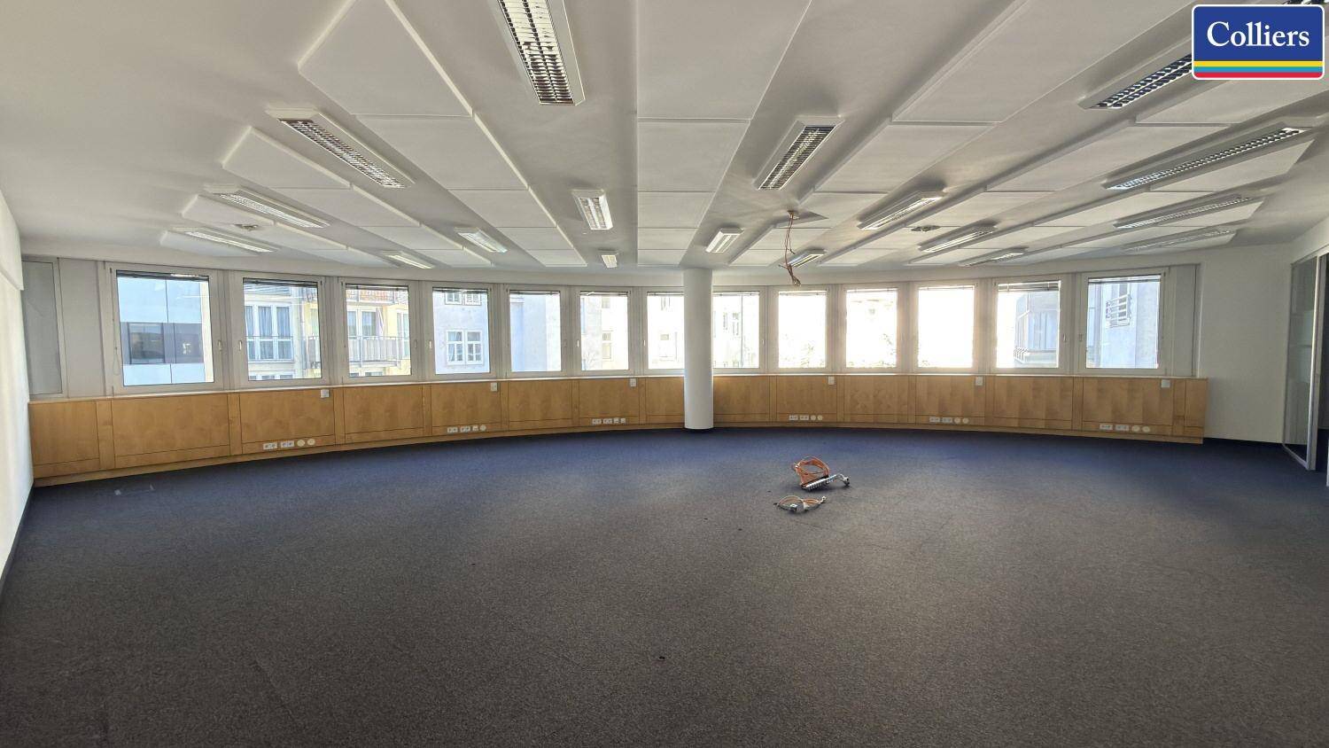 Großes, offenes Büro mit Teppichboden, vielen Fenstern und abgehängter Decke mit Beleuchtung.
