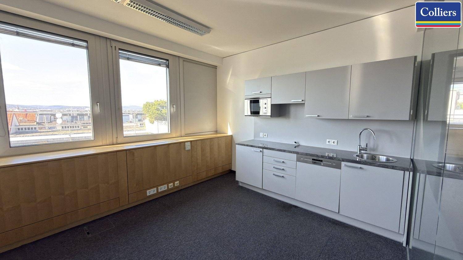 Moderne Küchenzeile in einem Büroraum mit Mikrowelle, Spüle und Blick nach draußen.
