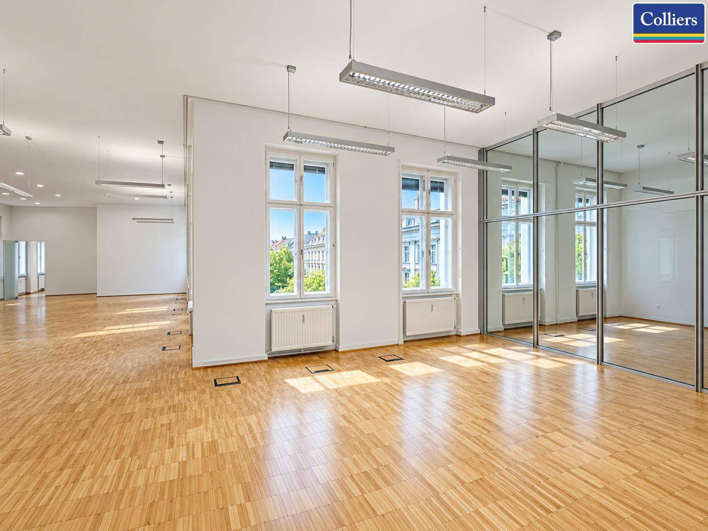 Großes Büro mit Parkettboden, Glaswänden und viel Tageslicht, perfekt für flexible Raumgestaltung.