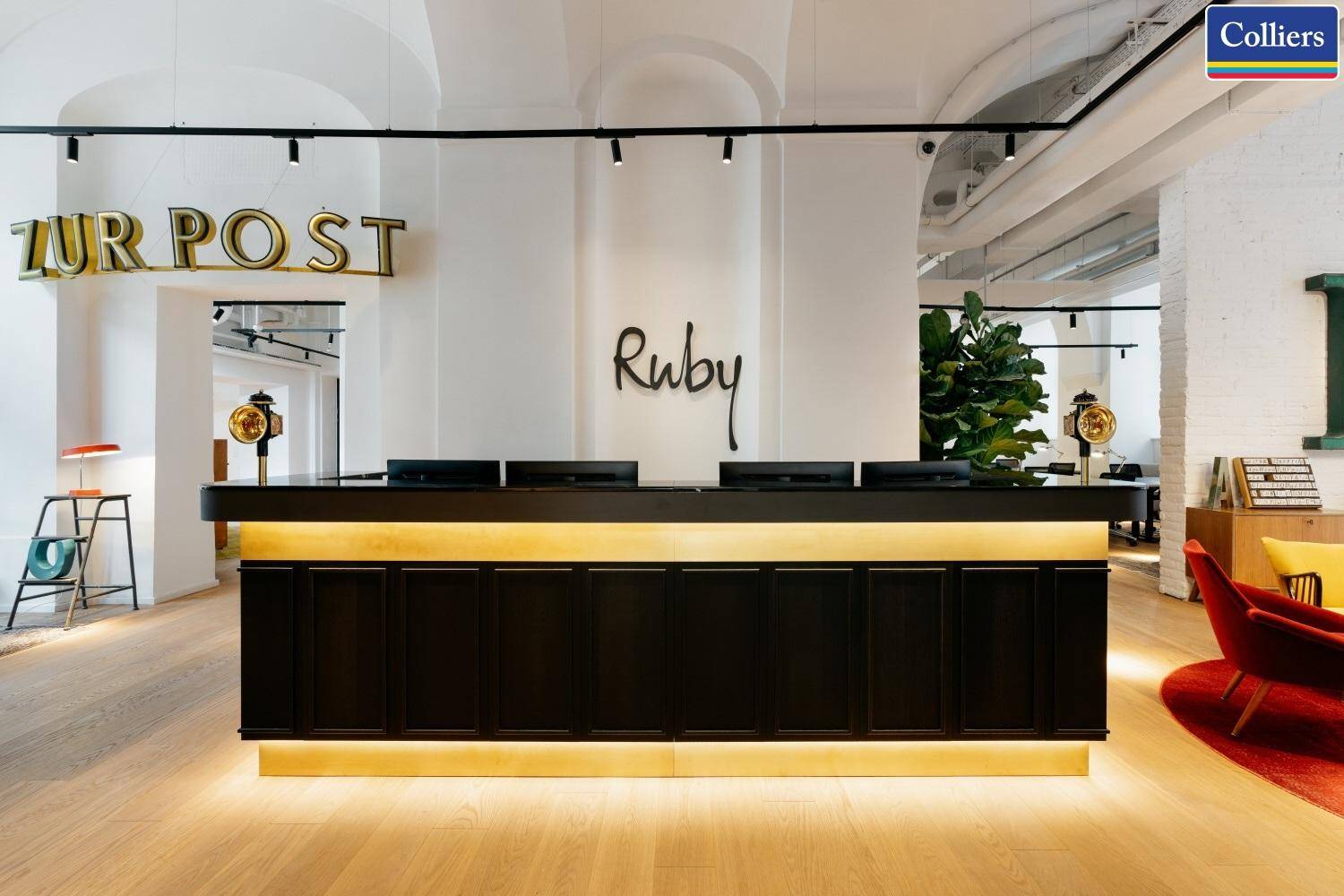 Moderner Empfangstresen mit beleuchteter Basis und dem Ruby-Logo an der weißen Wand.
