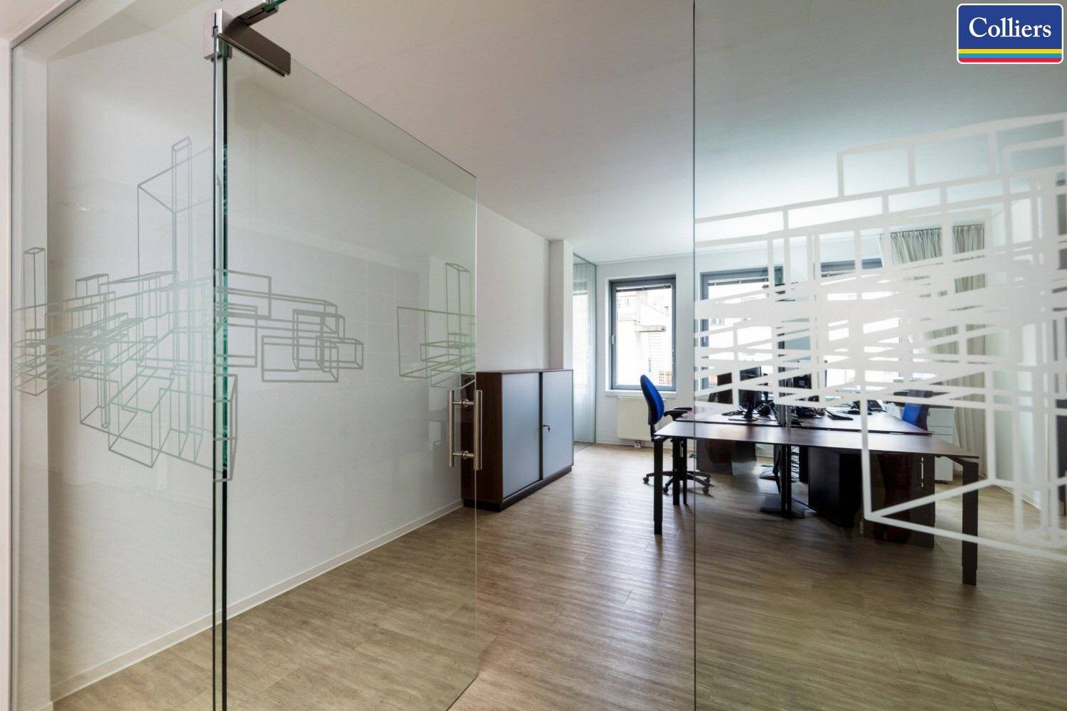 Moderner Büroraum mit Glaswänden und einem hellen Holzfußboden, der eine offene Arbeitsumgebung schafft.
