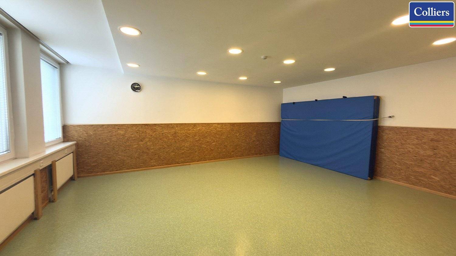 Vielseitiger Aktivitätsraum mit Sportmatte an der Wand, Einbaustrahlern und großen Fenstern für natürliches Licht.