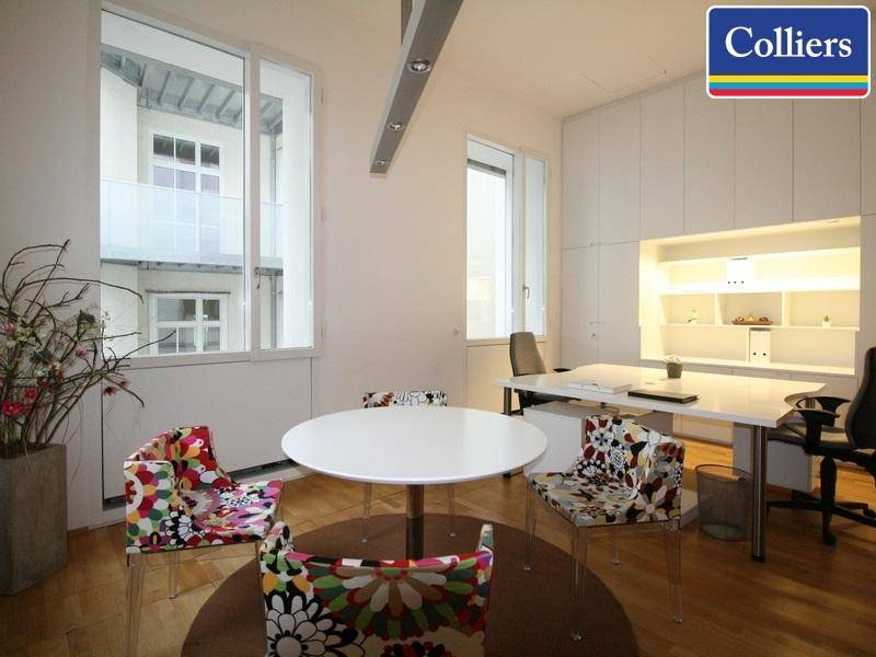 Helles Büro mit modernem Schreibtisch, bunten Stühlen und Blick auf einen ruhigen Innenhof.