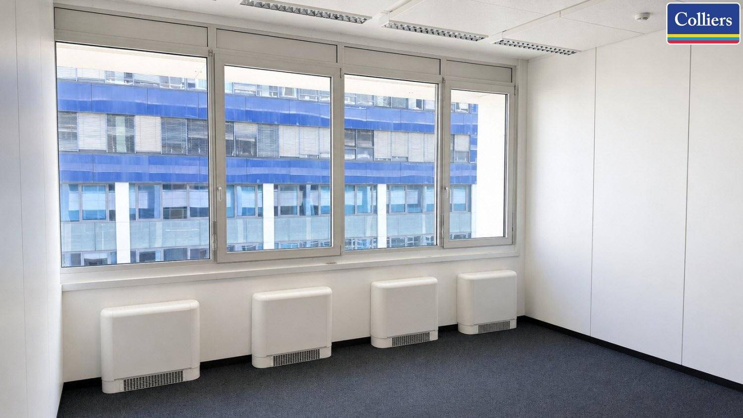 Helles Büro mit großen Fenstern, die einen Blick auf die Fassade eines anderen Gebäudes bieten.
