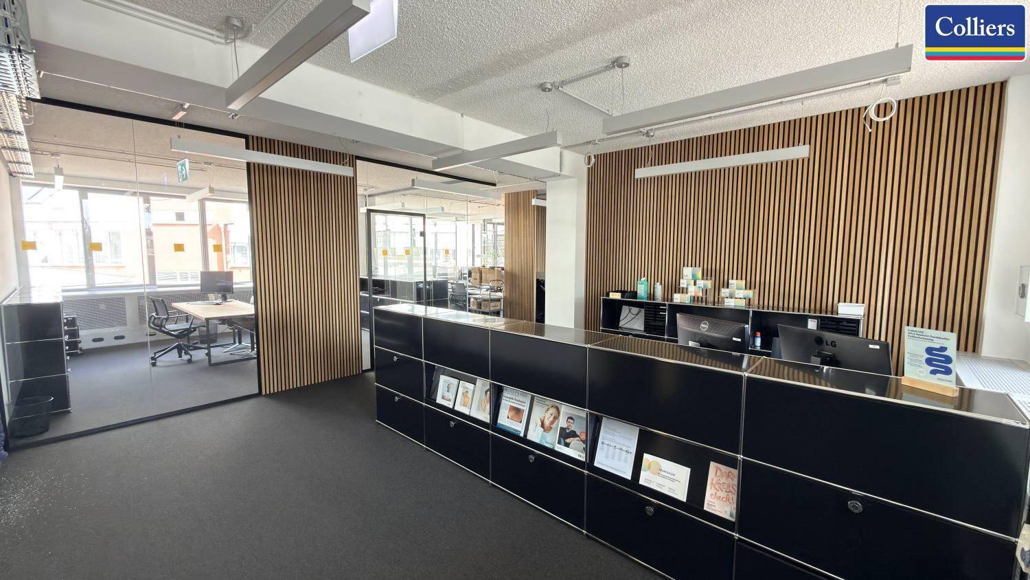Moderner Empfangsbereich in einem Büro mit Holzlamellenwand und dunklem Teppichboden.