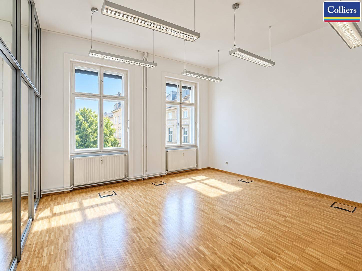 Helles Büro mit Parkettboden und großen Fenstern, die viel Sonnenlicht hereinlassen.