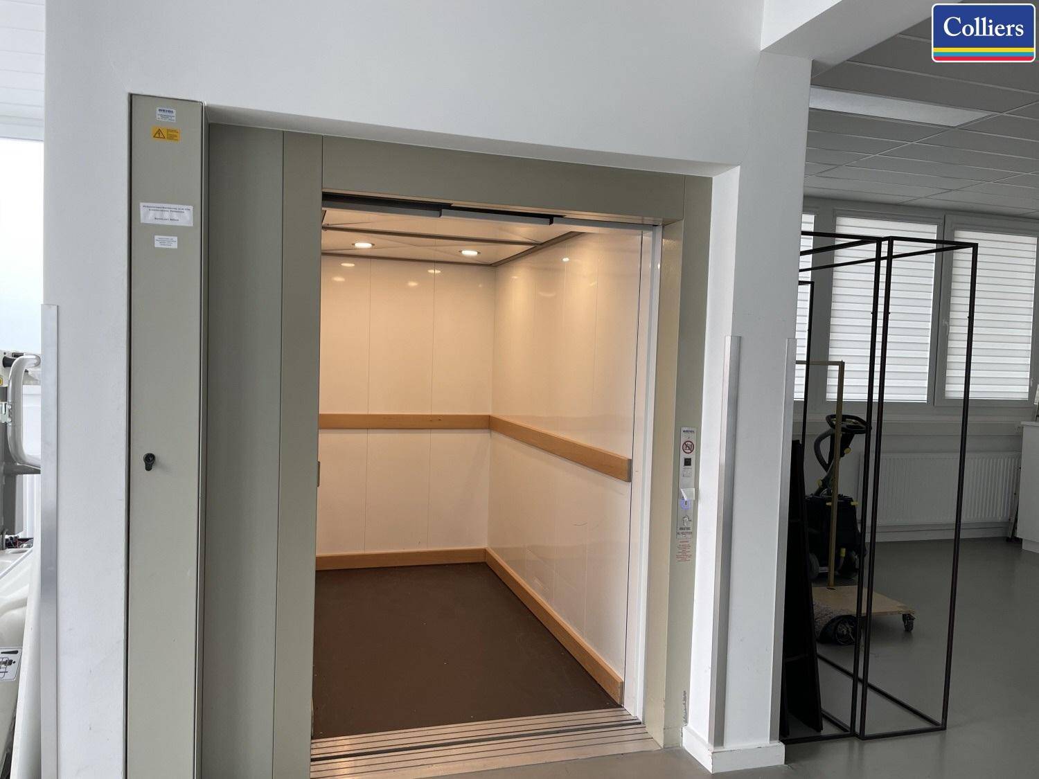 Geräumige Aufzugskabine mit heller Innenausstattung, Holzhandlauf und Metalltüren.