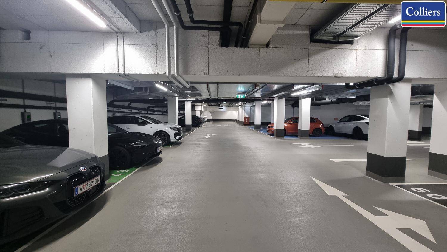 Tiefgarage mit vielen Parkplätzen, Beleuchtung und sichtbaren Rohren an der Decke.