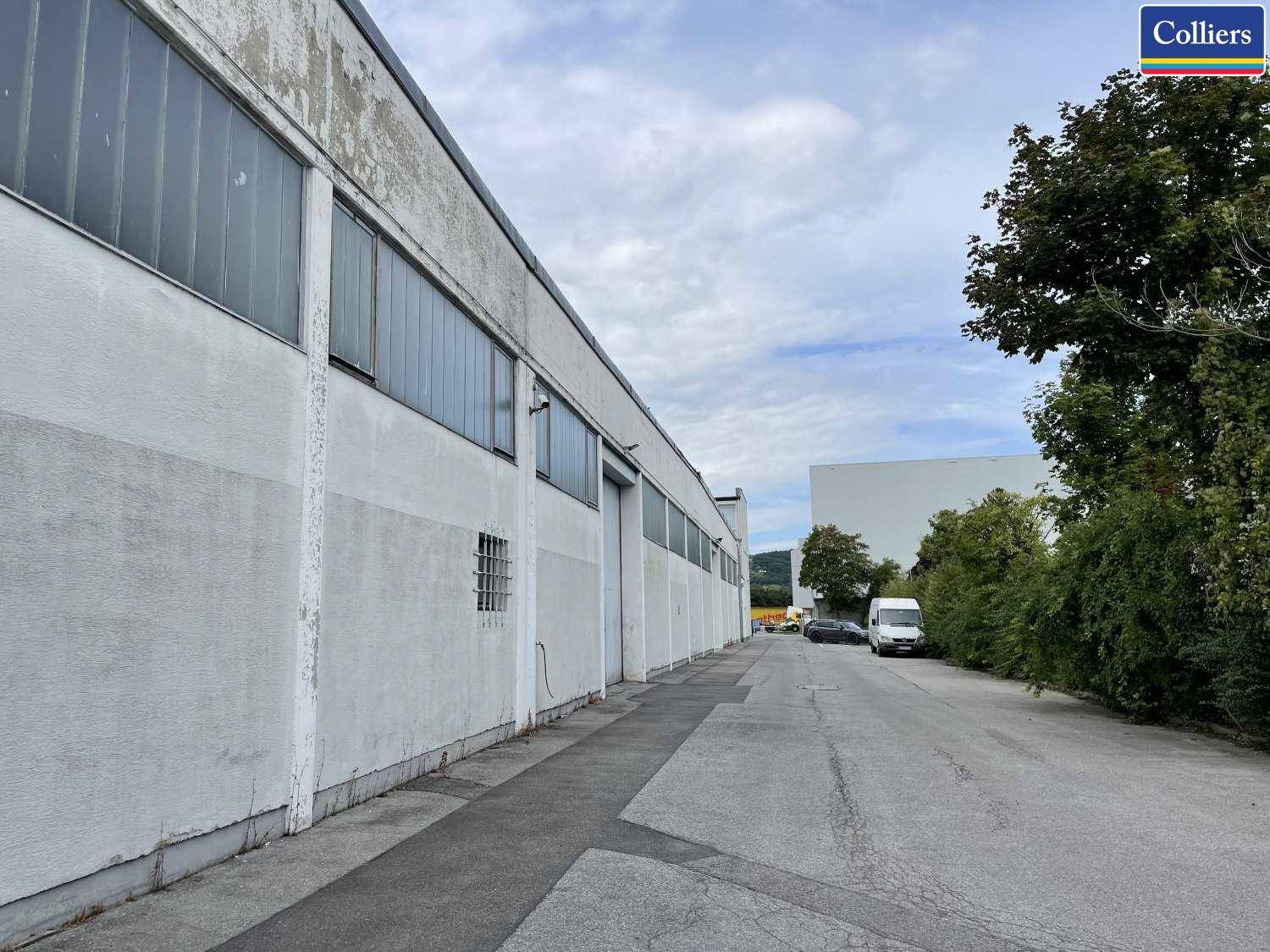 Seitenansicht einer langen Industriehalle mit vielen Fenstern und einer Zufahrtsstraße.