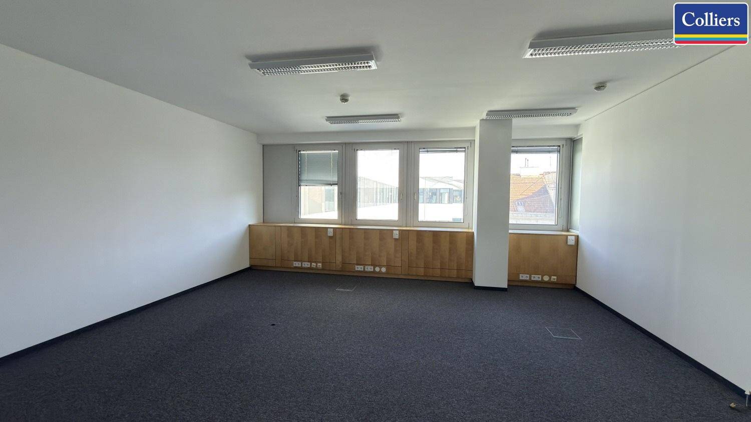 Großes, leeres Büro mit weißen Wänden, Teppichboden und Fenstern mit Blick nach draußen.