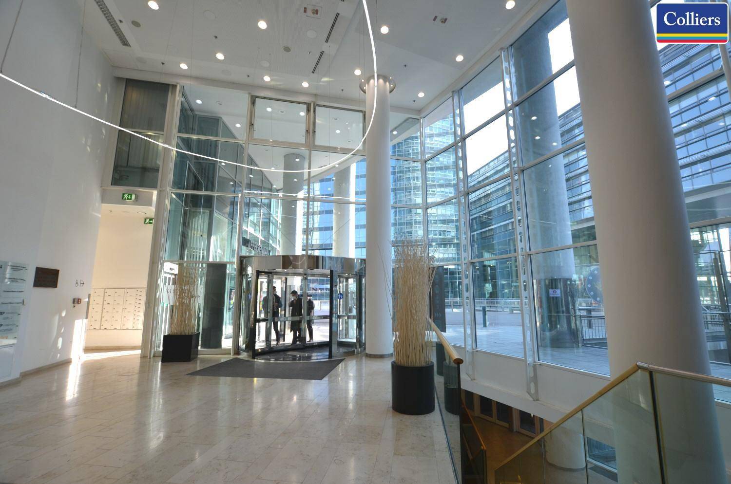 Moderne, lichtdurchflutete Lobby mit hohen Glasfassaden, Marmorboden und Drehtür, die einen einladenden Empfangsbereich schafft.