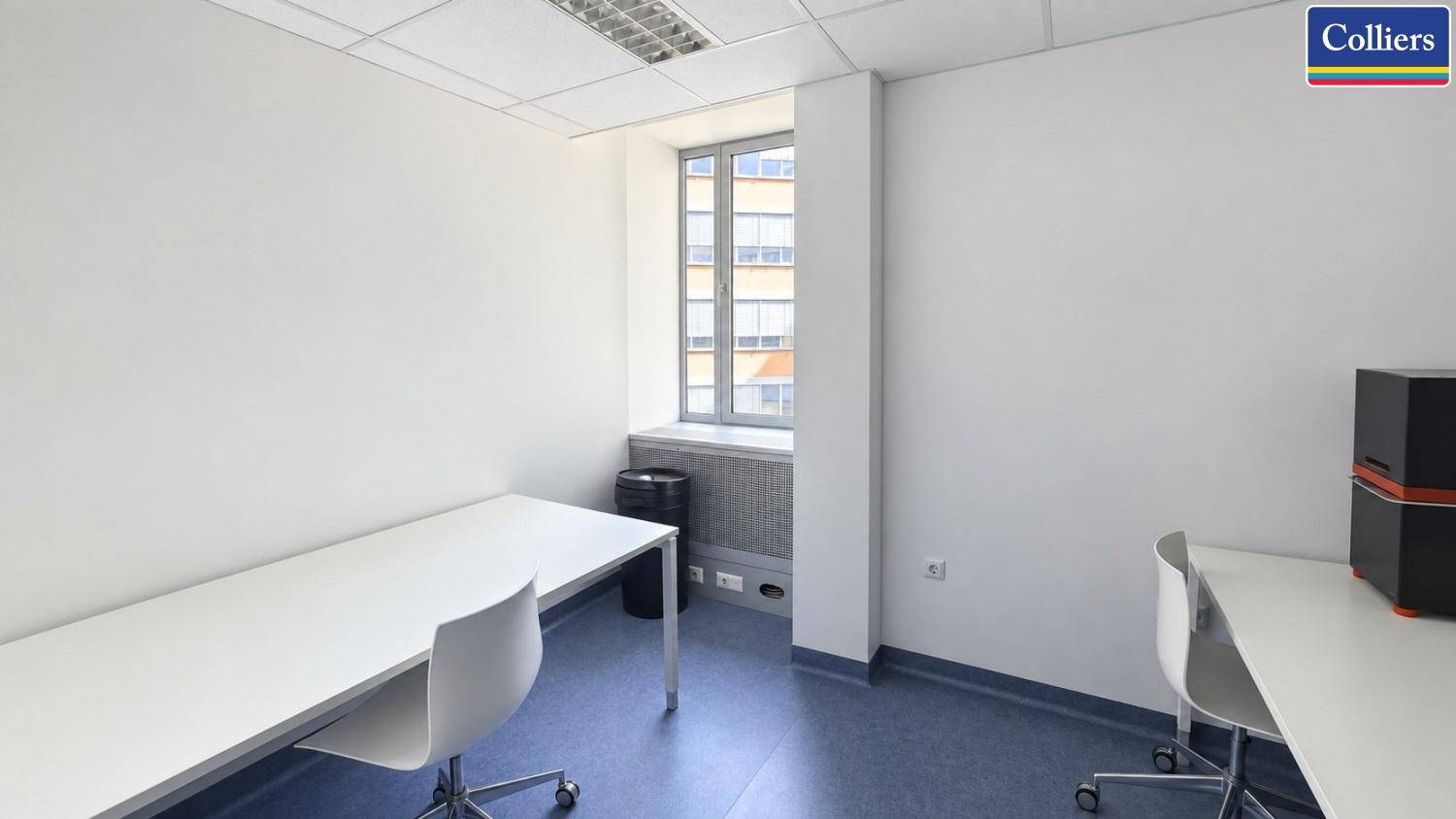 Kleines, helles Büro mit Schreibtischen und einem Fenster, das Tageslicht hereinlässt.