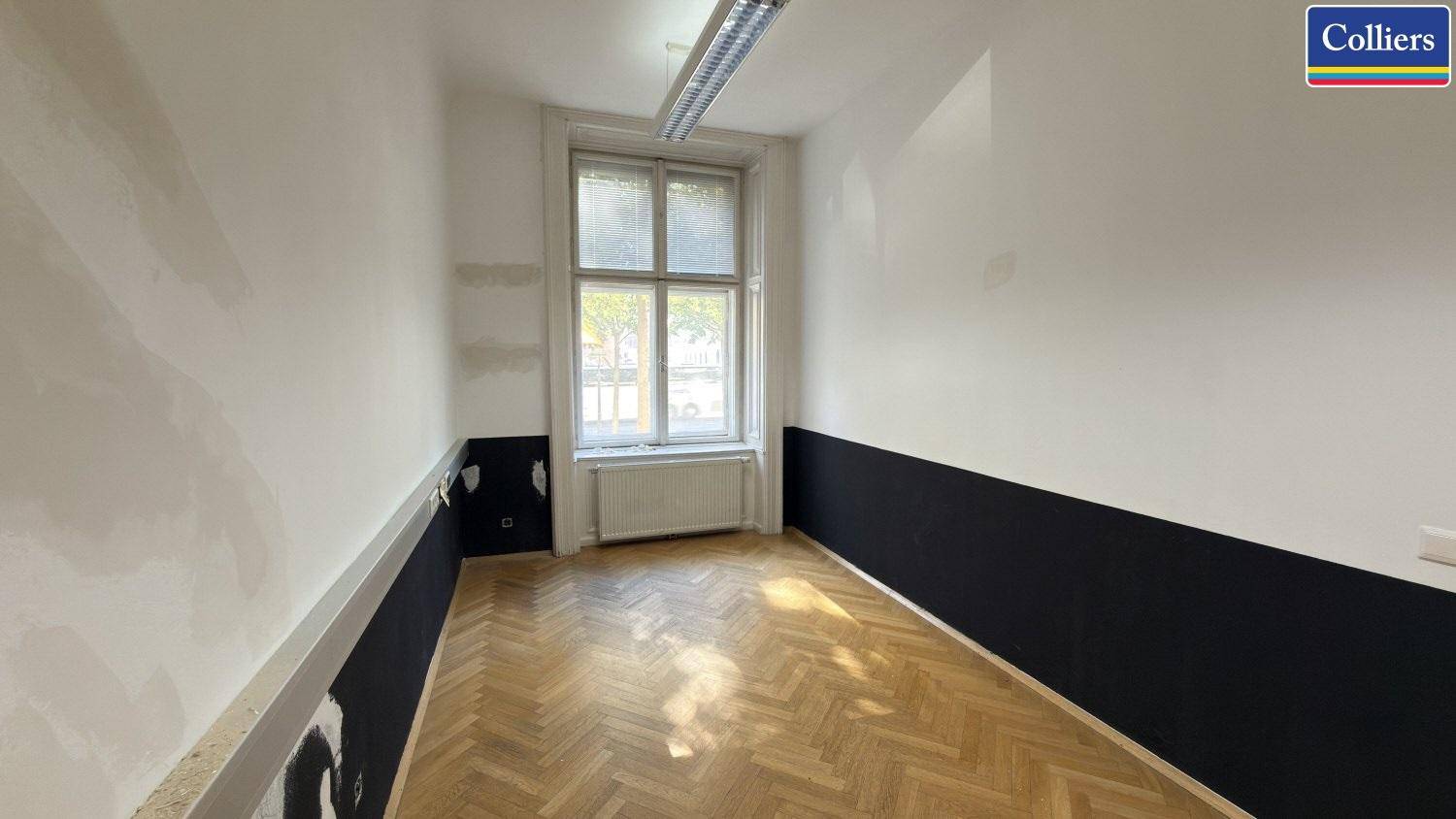 Schmaleres Büro mit Fischgrätparkett und großem Fenster, bietet Potenzial für eine effiziente Raumnutzung.