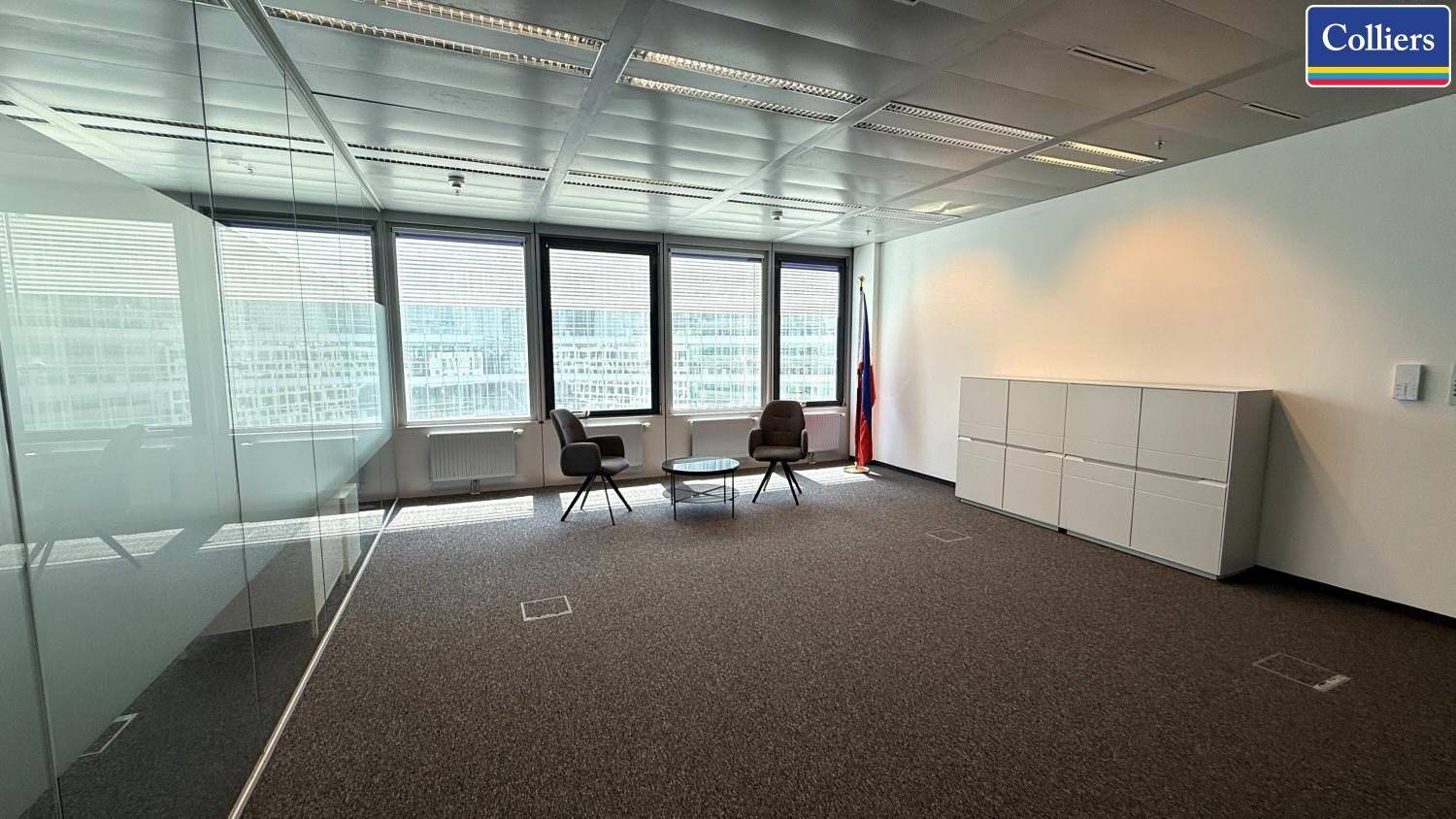 Geräumiges Büro mit Glaswand, kleiner Sitzecke und weißen Aktenschränken, ideal für Besprechungen.