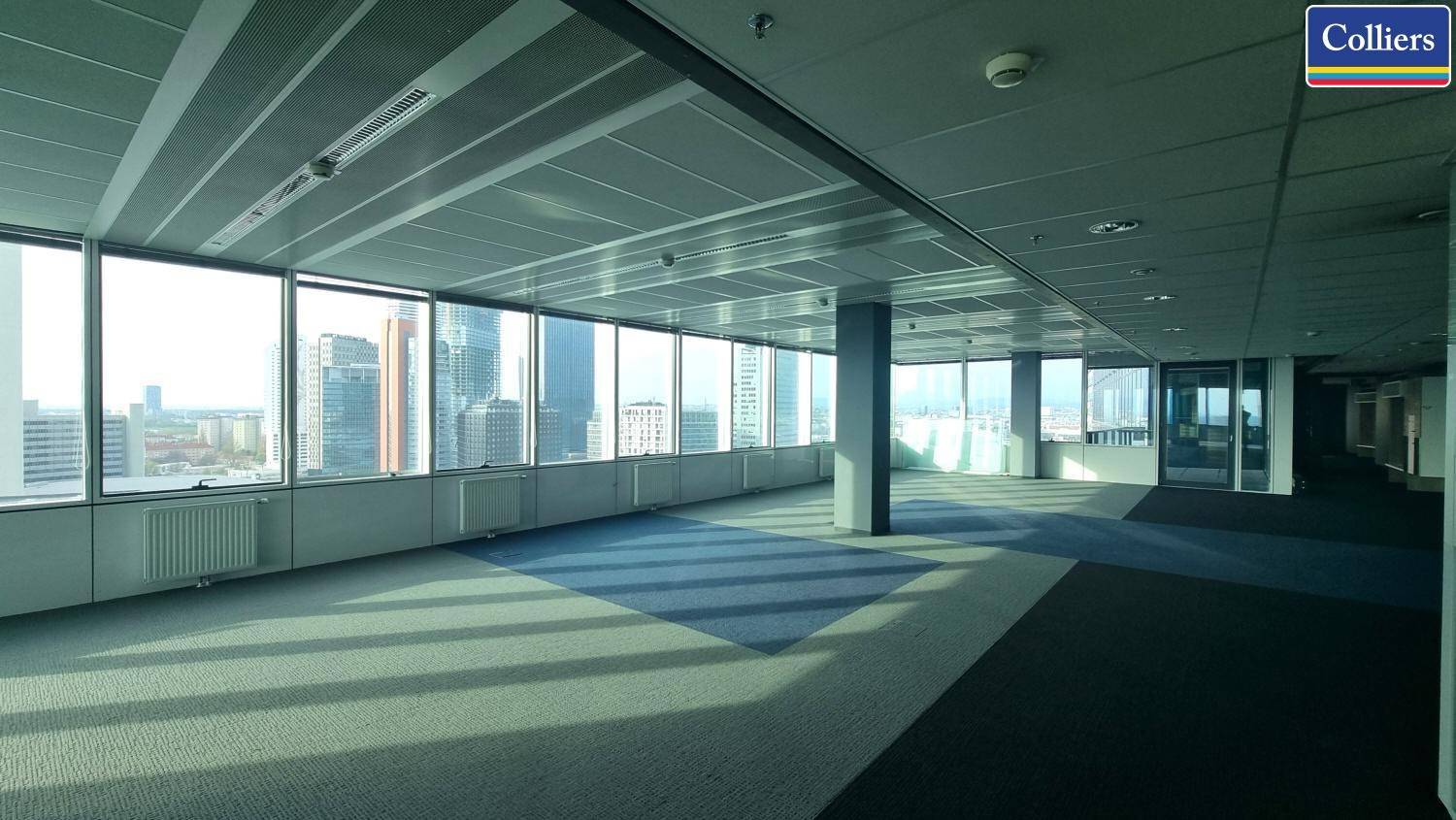 Geräumiges Büro mit Teppichfliesen und Säulen, bietet einen Panoramablick auf die Stadtlandschaft.