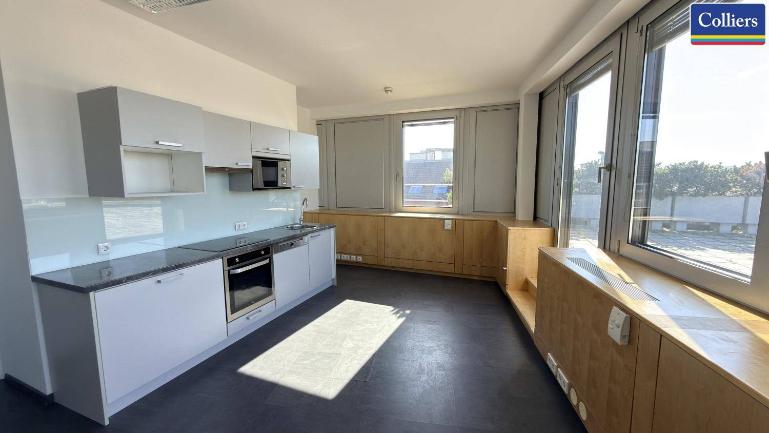 Funktionale Küchenzeile in einem Büroraum mit Kochfeld, Backofen und viel Tageslicht.