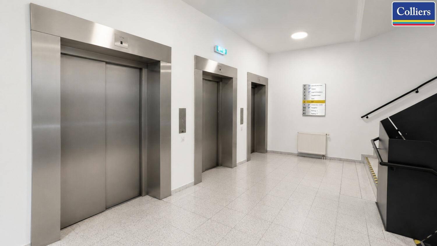 Eingangsbereich mit drei Aufzügen und einer Treppe, ausgestattet mit Fliesenboden.