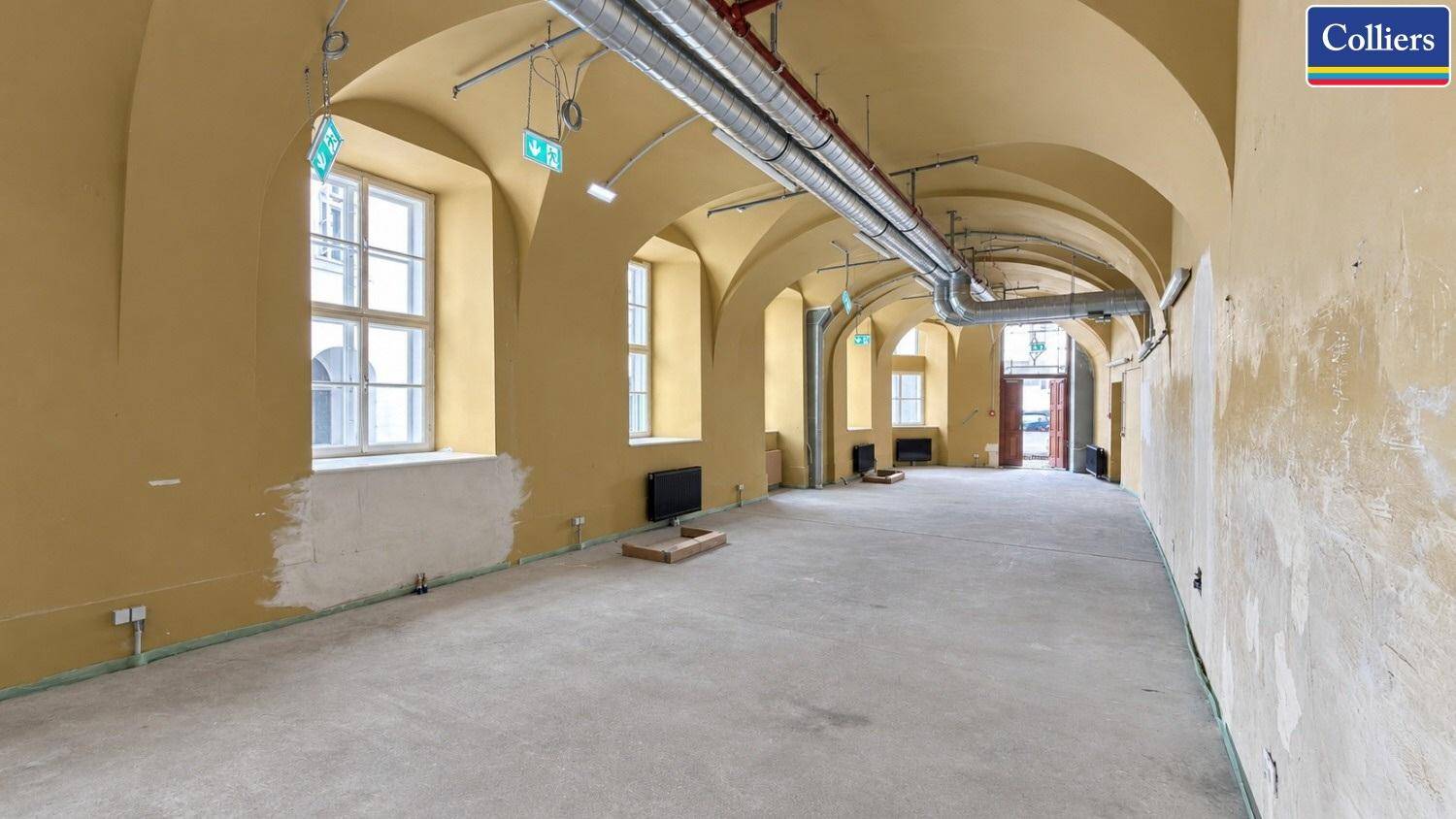 Langer, heller Raum mit beeindruckenden Gewölbedecken, freiliegenden Installationen und großen Fenstern.