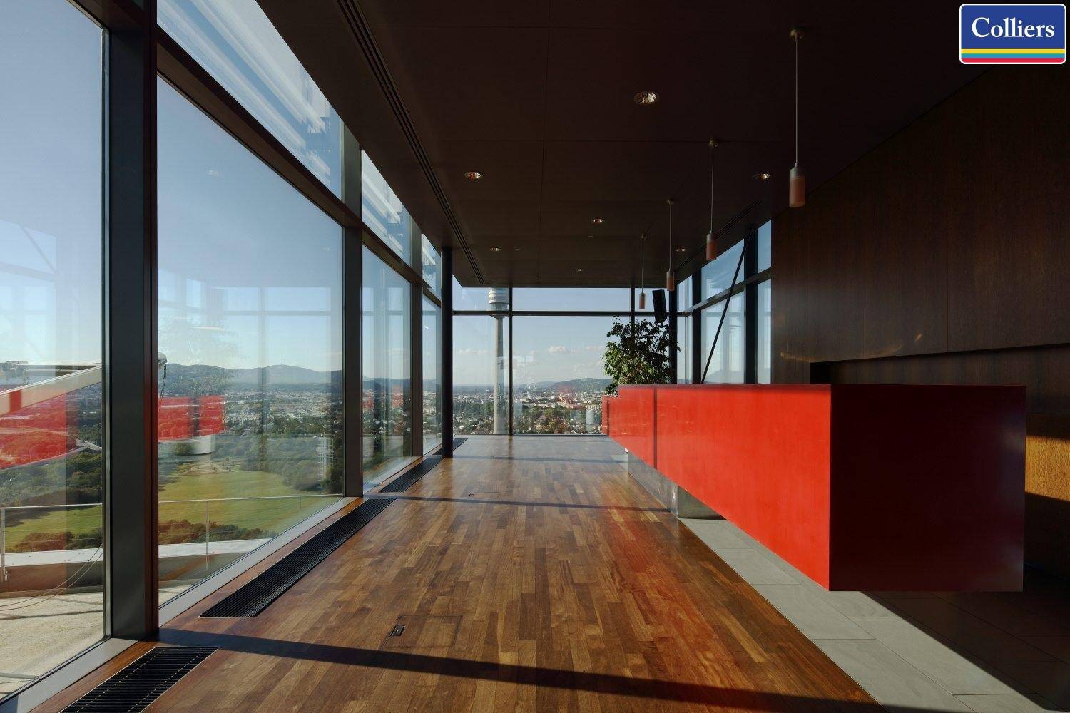 Moderner Empfangsbereich mit Holzboden, großen Glasfronten und einer auffälligen roten Theke.