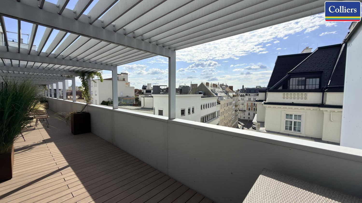 Weitläufige Dachterrasse mit Holzdeck, Pergola und Blick auf die umliegenden Gebäude der Stadt.
