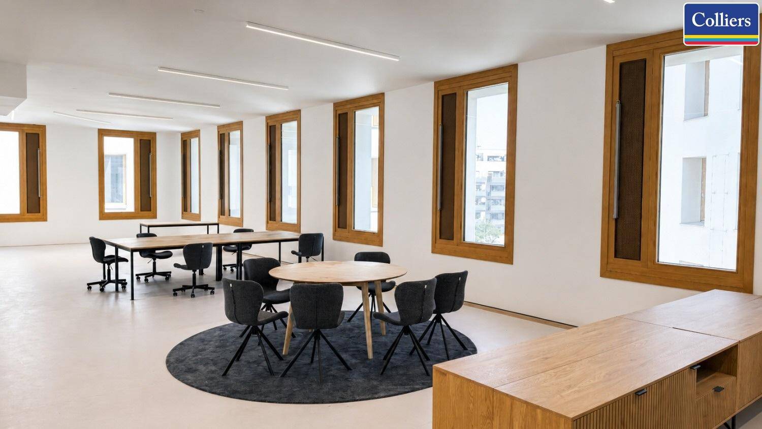 Offener Bürobereich mit runden und rechteckigen Tischen, ergonomischen Stühlen und großen Fenstern.