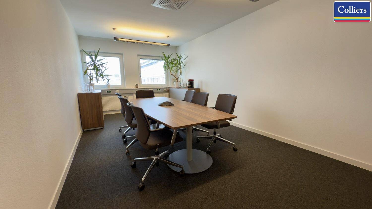 Funktionaler Besprechungsraum mit Teppichboden, einem Holztisch und Fenstern für Tageslicht.