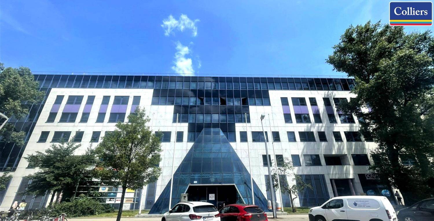 Moderne Bürogebäude-Fassade mit großen Glasflächen und weißen Elementen unter blauem Himmel.