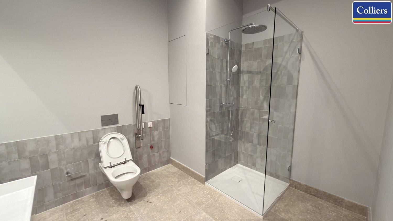 Modernes Badezimmer mit barrierefreier Dusche, Wand-WC und Haltegriffen, in neutralen Grautönen gefliest.