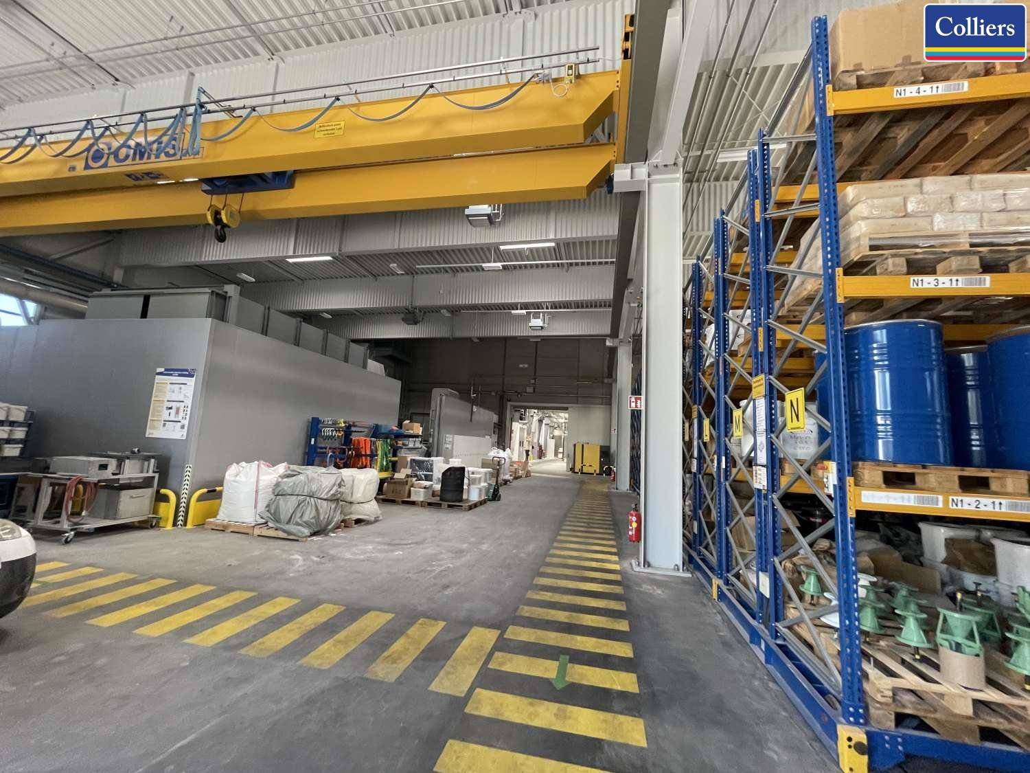 Langer Gang in einer Lagerhalle mit hohen Regalen, industrieller Beleuchtung und einem Kran.