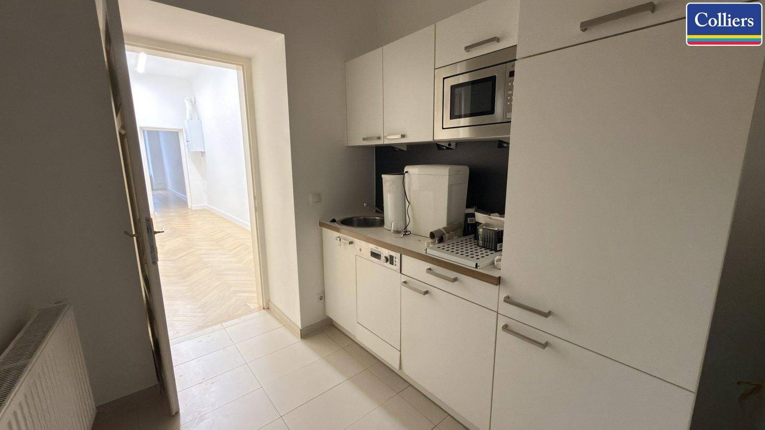 Funktionale Küchenzeile mit weißen Schränken, Mikrowelle und Spülmaschine, ideal für Büroflächen.