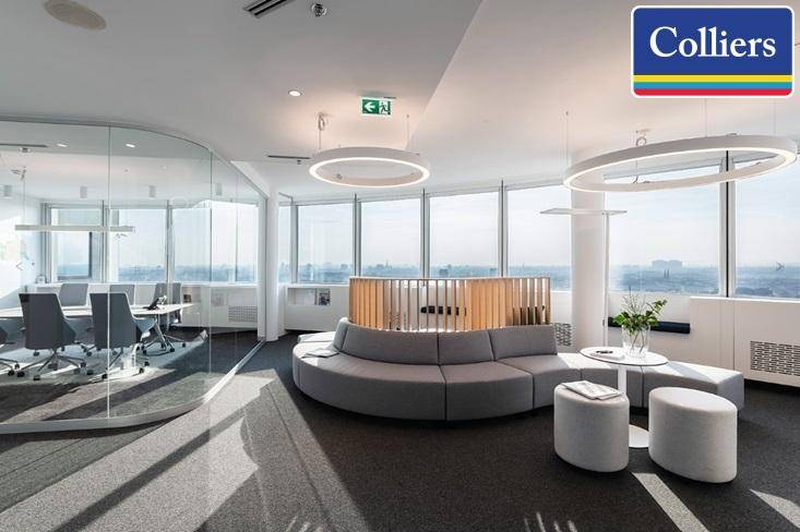 Moderner Büroloungebereich mit geschwungenem Sofa, runden Tischen und Glaswänden mit Stadtblick.