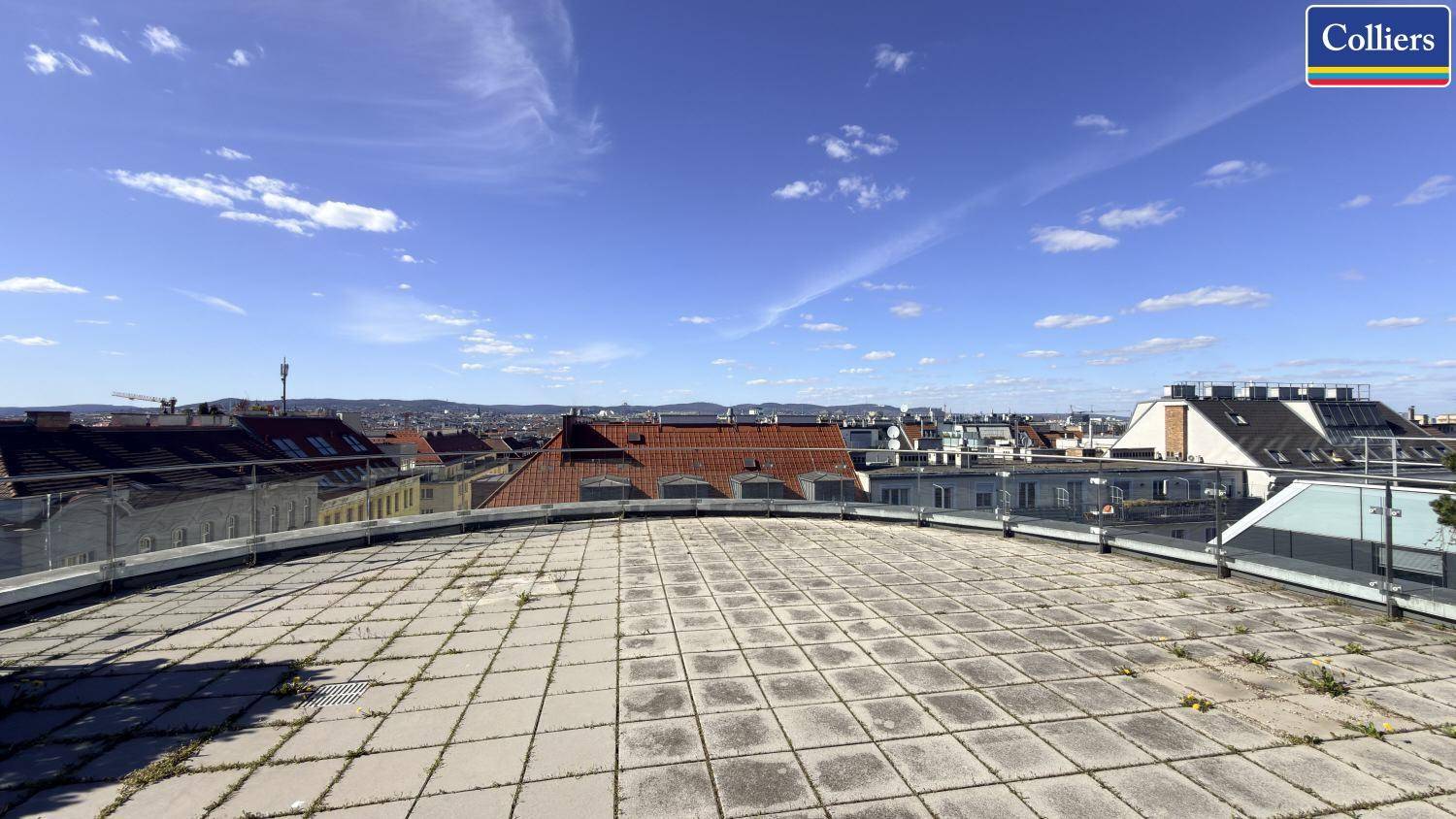 Große Dachterrasse mit Steinplatten und weitem Blick über die Dächer der Stadt.