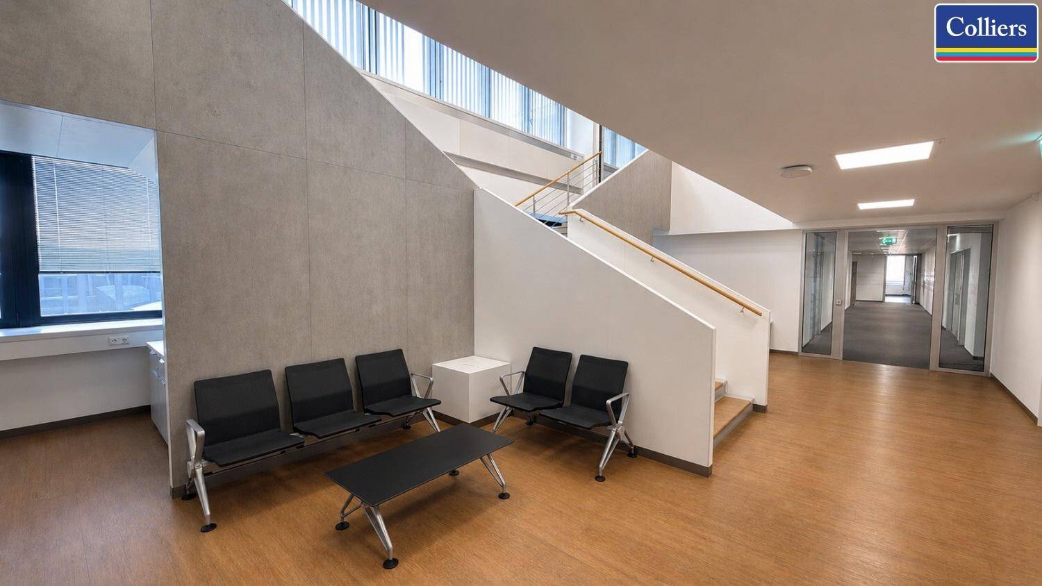 Geräumiger Flur mit Treppenaufgang, Wartebereich und Holzfußboden, verbindet verschiedene Bürobereiche.