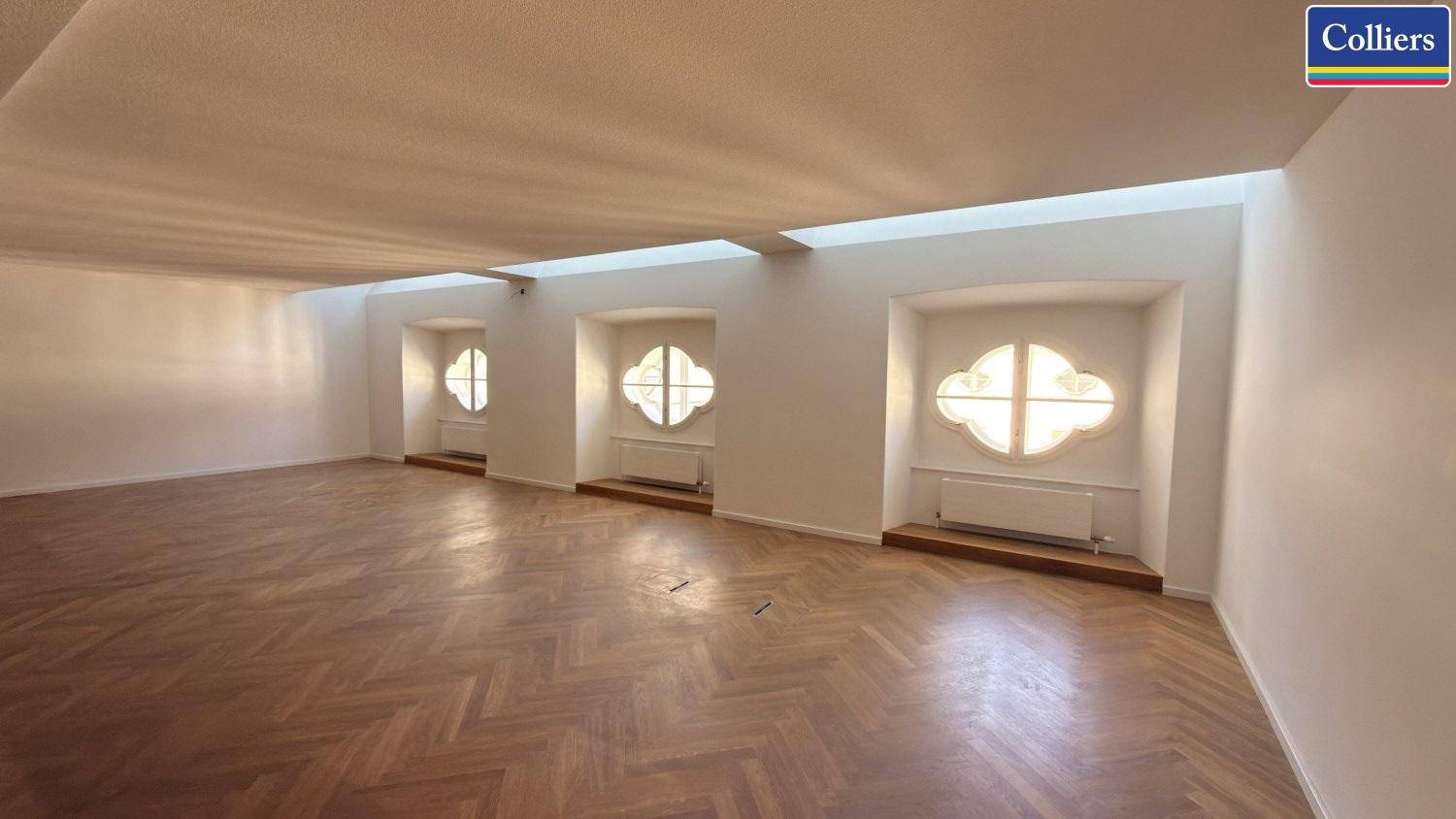 Heller Büroraum mit elegantem Fischgrätparkett und dekorativen Fenstern, die viel Tageslicht hereinlassen.