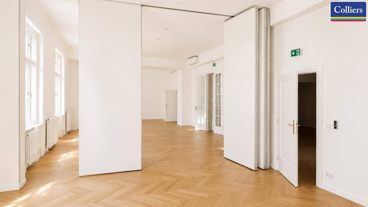 Flexibler Bürobereich mit mobilen Trennwänden, Fischgrätparkett und hohen Decken für vielseitige Nutzung.